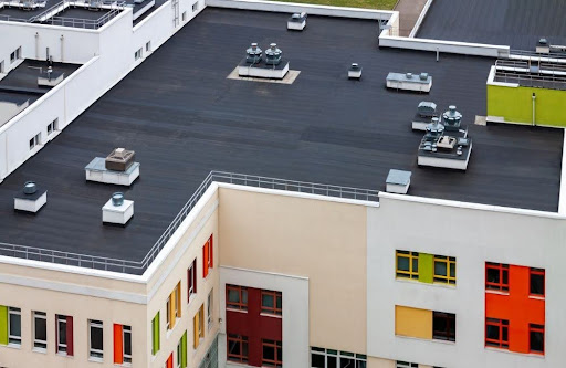 Flat rooftop of a modern building with multiple vents and HVAC units; building exterior features colorful window frames in red, yellow, and green.