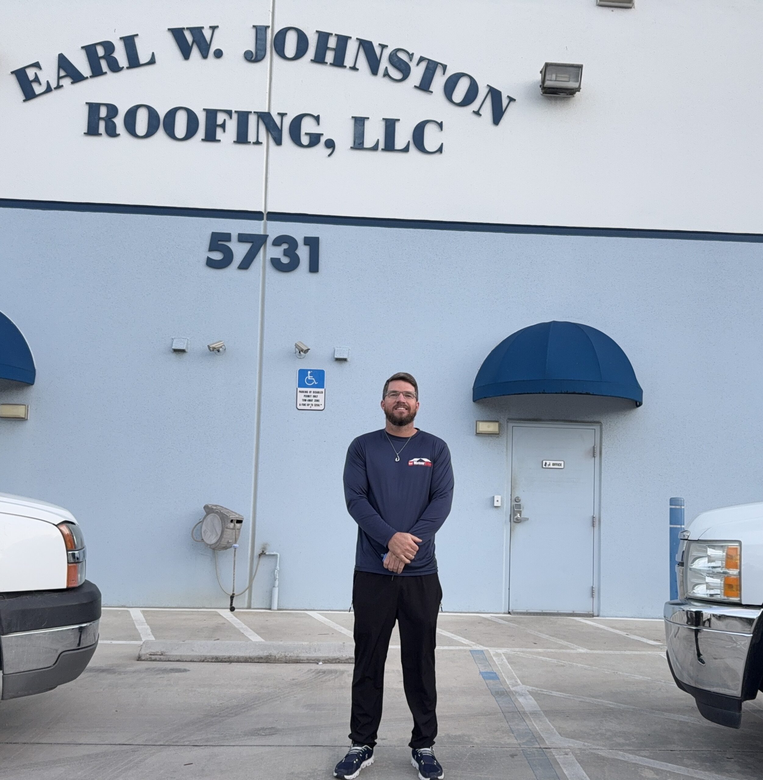 A man stands in front of a building labeled "Earl W. Johnston Roofing, LLC" with the street number 5731 visible above him. Two trucks are parked on either side.