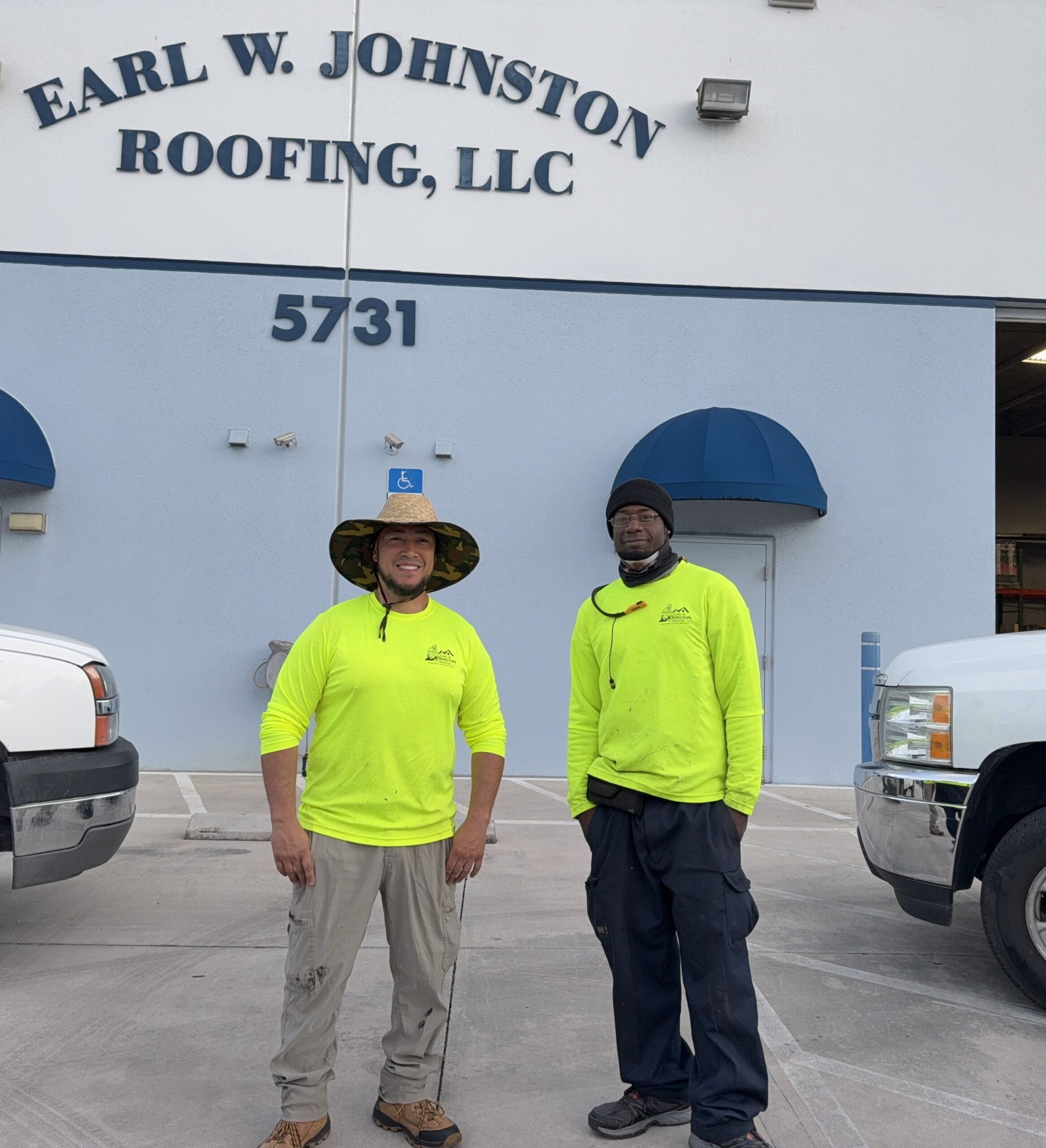 Two workers in neon yellow shirts stand in front of the Earl W. Johnston Roofing, LLC building, address 5731, with two white trucks parked nearby.